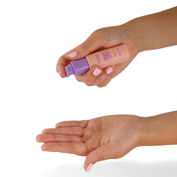 With light pink nail polish, a person dispenses evre.s Bright & Early Vitamin C Repair Serum from a peach and purple tube onto their open palm against a plain white background.