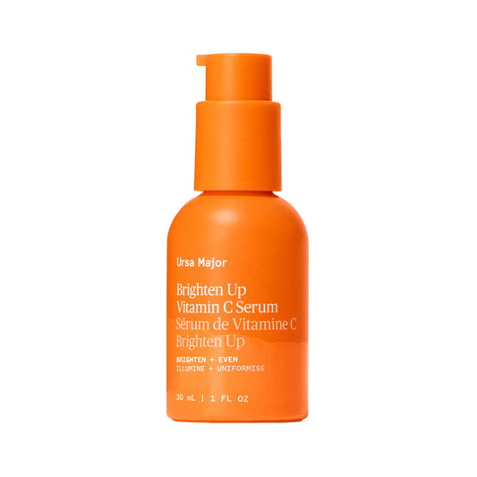 An orange bottle of Ursa Major Brighten Up Vitamin C Serum with a pump and white text highlights its featherweight hydration, brightening, and even skin tone benefits.
