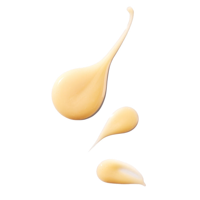 Three drops of Ursa Major’s Brighten Up Vitamin C Serum, in a creamy light beige, are displayed on a white background. The largest drop is teardrop-shaped with a long tail; the other two are smaller with smooth, glossy textures.