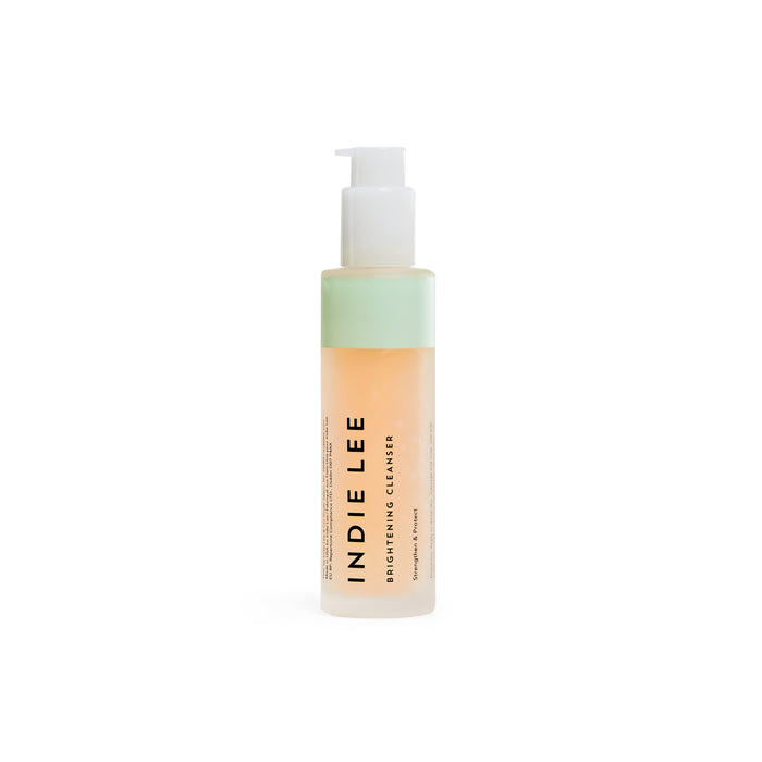 The Indie Lee Brightening Cleanser features a clear bottle with a pump, revealing its antioxidant-rich orange liquid. Its white label with black text highlights promises of effective skin brightening.