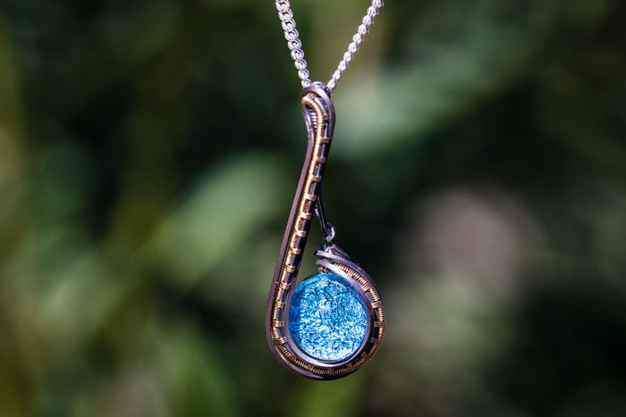 Copper wire wrapped pendant with a blue infused glass cabochon on a silver chain.