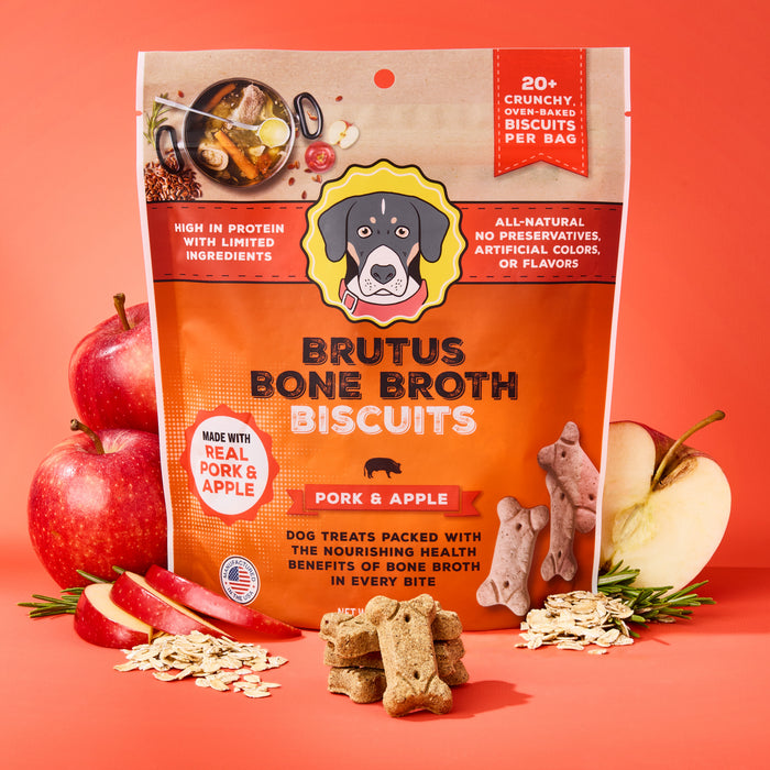 The Pork & Apple Brutus Bone Broth Biscuits by Brutus Broth feature real meat and bone broth, highlighting joint health benefits. The package, set against an orange backdrop surrounded by apples, oats, and treats, stands out with its vibrant design.