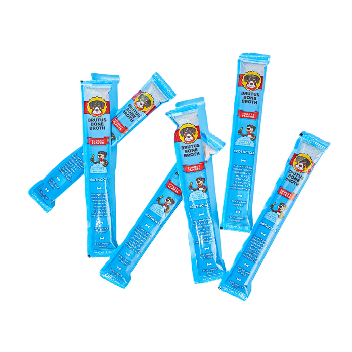 Six blue sticks of Brutus Brothcicles, by Brutus Broth, are randomly arranged. The packaging displays a cartoon dog and product details in a red and blue design, highlighting these all-natural canine popsicles made with superfood ingredients to delight your dog.