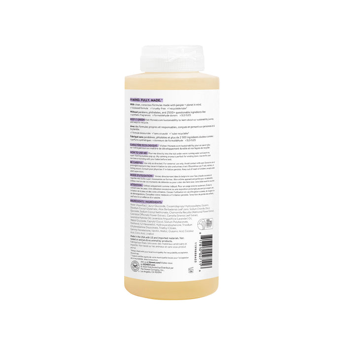 A bottle of Bubble Bath from The Honest Company features a beige liquid with a white cap and a detailed label showing instructions and product info in black and purple on a soothing plain white background, inviting relaxation with its calming properties.