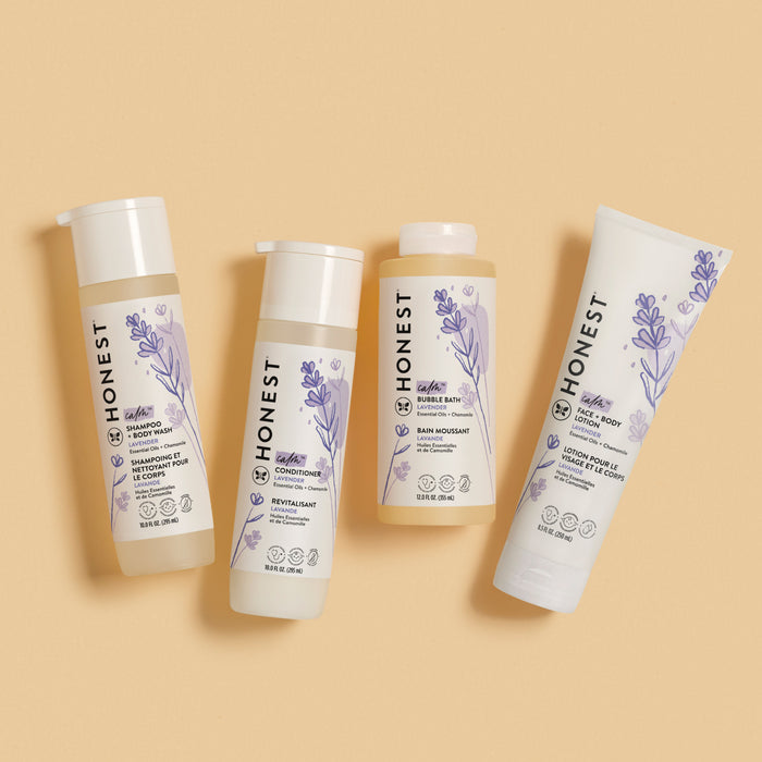 Four products from The Honest Company—shampoo, conditioner, bubble bath, and face/body lotion—are displayed on a beige background. Each bottle is adorned with lavender illustrations and bilingual English and French text. The bubble bath features soothing chamomile extract.