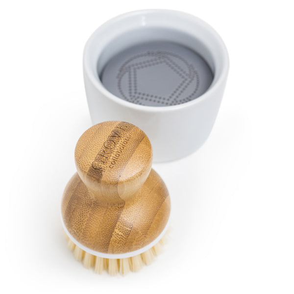 A Grove Co. Bubble Up Dish Soap Dispenser & Brush Set includes a chic wooden brush with light bristles and a small round white container filled with gray soap, perfect for your dishwashing needs.