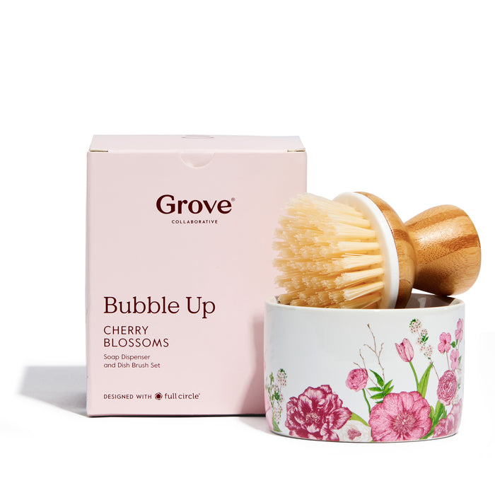 The Grove Co. Bubble Up Dish Soap Dispenser & Brush Set includes a wooden-handled dish brush and a white ceramic dish with pink and red floral designs.