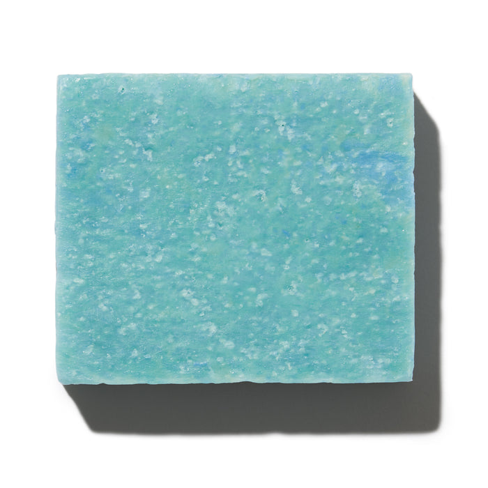 The NOT!CE Hair Co Bubble-Yum Body Bar, a square light blue soap on a white background, highlights its vegan, cruelty-free nature. Its textured surface with subtle color variations casts a gentle shadow bottom-left.