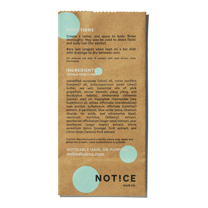 The Bubble-Yum Body Bar from NOT!CE Hair Co comes in brown paper packaging with turquoise dots, listing vegan and cruelty-free ingredients. Instructions include lathering and rinsing this plastic-free hair care product. Learn more at noticehairco.com.