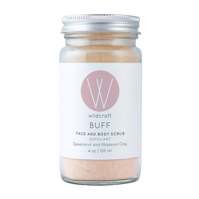 The Buff Face and Body Scrub by Wildcraft comes in a glass jar and contains a light pink exfoliator with spearmint and rhassoul clay, offering a natural scent. The 4 oz (120 ml) jar is elegantly finished with a sleek metal lid.