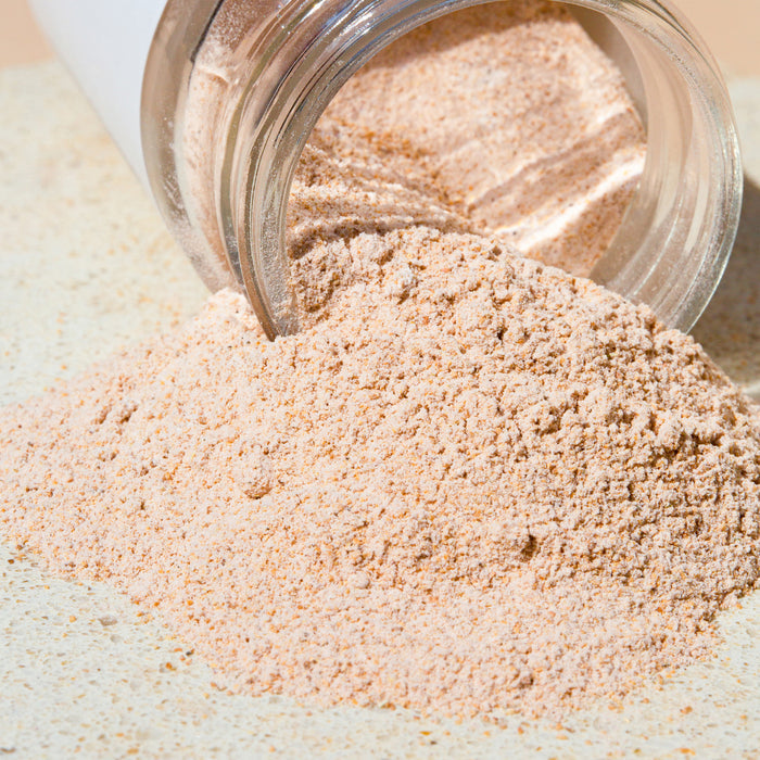 A jar tipped over, spilling the soft, beige Buff Face and Body Scrub by Wildcraft onto a light surface. Its grainy texture and natural scent make it ideal for skin revitalization.
