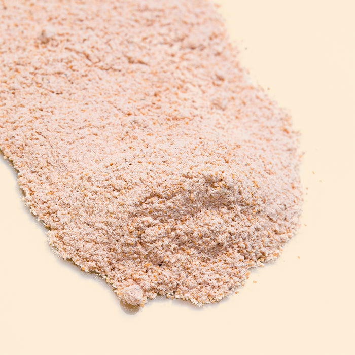 A close-up captures Buff Face and Body Scrub by Wildcraft, featuring a fine, exfoliator-like texture of light brown powder spread across a beige surface with its natural scent.
