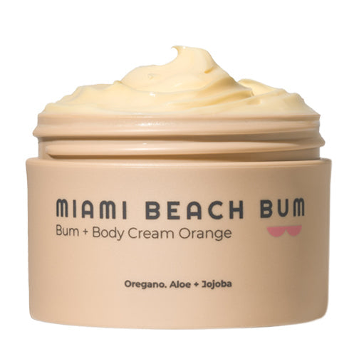An open Miami Beach Bum Bum + Body Cream jar displays a swirl of orange-colored cream designed for skin health. The beige jar, featuring a small pink design, lists ingredients such as oregano, aloe, and jojoba.