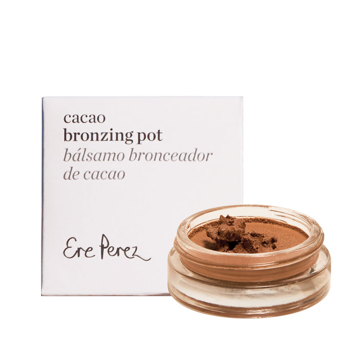 An open small glass pot of cocoa-colored bronzing balm reveals a hint of face bronzer. Behind it, a white box shows Cacao Bronzing Pot and Bálsamo Bronceador de Cacao with the Ere Perez brand, promising a natural glow.