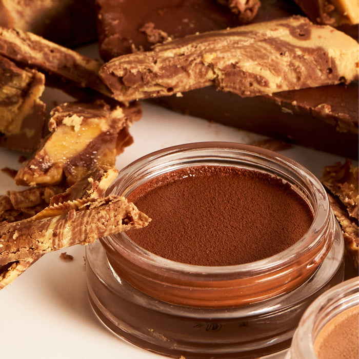 A glass container with creamy chocolate mousse is accompanied by marbled chocolate bark that echoes the swirled allure of Ere Perezs Cacao Bronzing Pot, crafting an indulgent dessert scene.