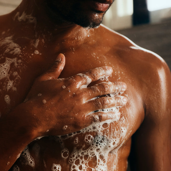 A close-up of a person washing their chest with Oars + Alps Cali Coast Body Wash, rich in Vitamin E and antioxidants. The fresh California Coast scent evokes cleanliness and self-care.