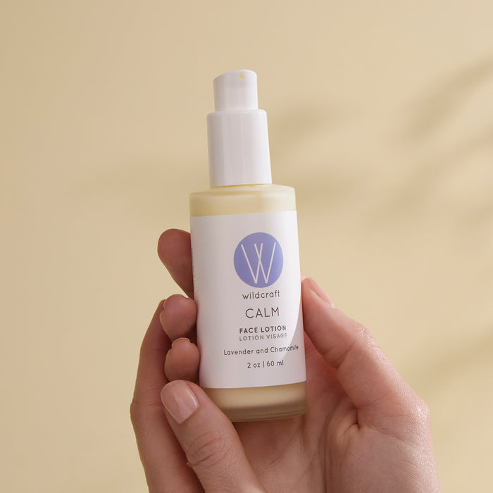 A hand holds Wildcraft Calm Face Lotion, a lightweight moisturizer with lavender and chamomile, shown in a pump bottle with a pale purple label against a beige background.