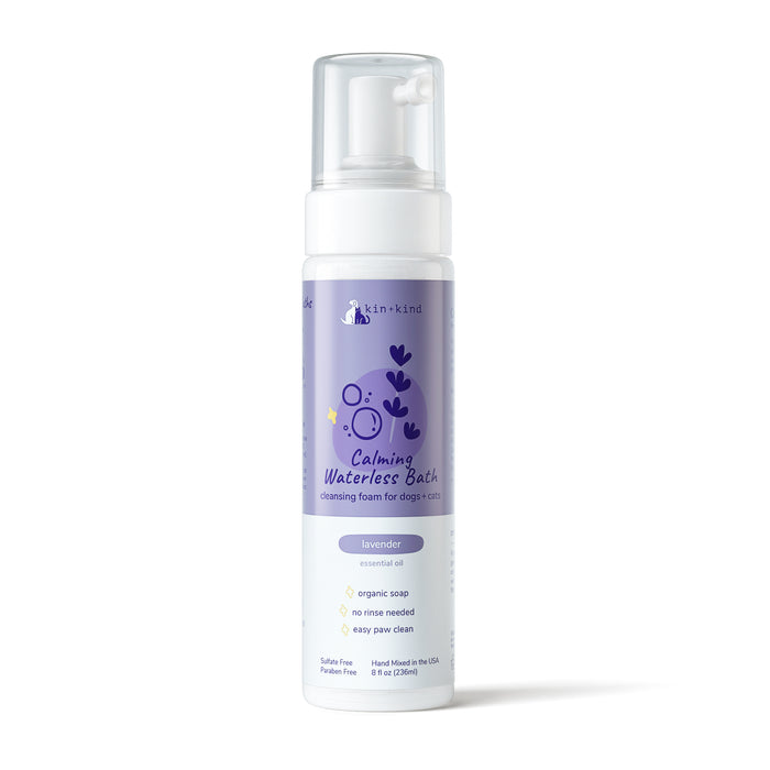 The kin+kind Calming Lavender Waterless Bath for Cats & Dogs in an 8 fl oz purple bottle with pump dispenser emphasizes natural pet care. The label depicts a dog, features organic soap with a lavender scent, requires no rinse, and is ideal for easy paw cleaning. Its sulfate-free and paraben-free.