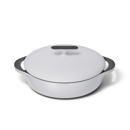 The Caraway Cast Iron Braiser with Lid, 3.5 qt, is a white enameled dish featuring rounded handles and a flat handle on the lid. It offers superior heat retention with a sleek, modern design and smooth glossy finish.