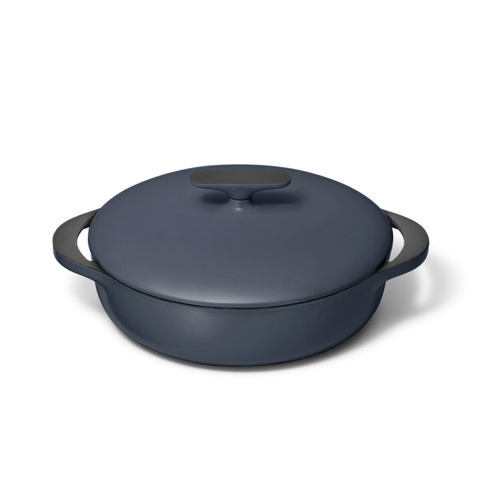The Caraway Cast Iron Braiser with Lid, 3.5 qt, in dark gray enamel features superior heat retention and durability. It has two side handles and a small lid handle, beautifully set against a white background.