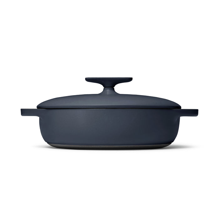 The Caraway Cast Iron Braiser with Lid, 3.5 qt, in matte black features a round knob and dual side handles, set against a white background. Known for its excellent heat retention, this durable dish is perfect for any kitchen.