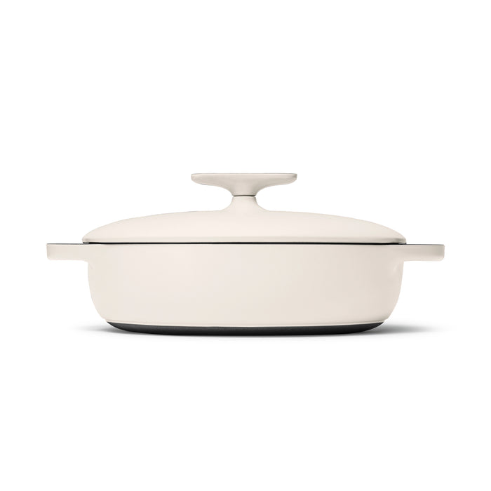 A 3.5 qt cream-colored Caraway cast iron braiser with a lid and side handles is shown against a white backdrop. It offers excellent heat retention due to its smooth, durable enamel coating and rounded edges.