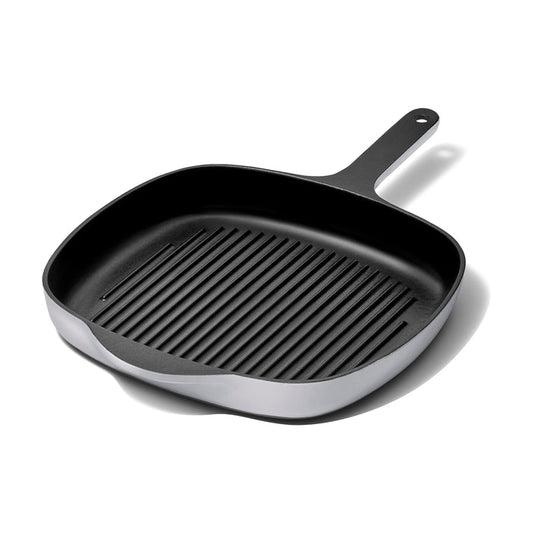 The 10.5 Caraway Cast Iron Grill Pan, with excellent heat retention and a non-stick black surface featuring raised ridges and a long handle, is shown diagonally on a white background.