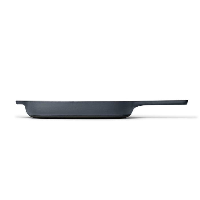 The Caraway Cast Iron Grill Pan, 10.5, in a sleek black enamel finish with a long handle, exhibits superior heat retention when viewed from the side against a white background.