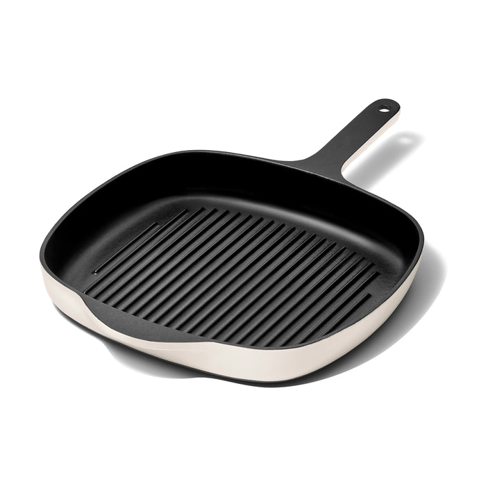 The Caraway Cast Iron Grill Pan, 10.5, features a black enameled square design with a white exterior and long handle. Its interior has raised ridges for grilling and excellent heat retention, all elegantly highlighted on a plain white background with a subtle shadow.