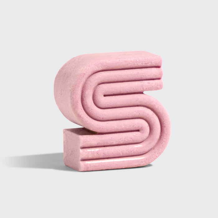 A pink, textured sculpture in the shape of an S stands against a light gray background. Its smooth, layered finish mirrors the sheen of Kitschs Castor Oil Nourishing Shampoo Bar, with a soft appearance and a gentle shadow to the left.