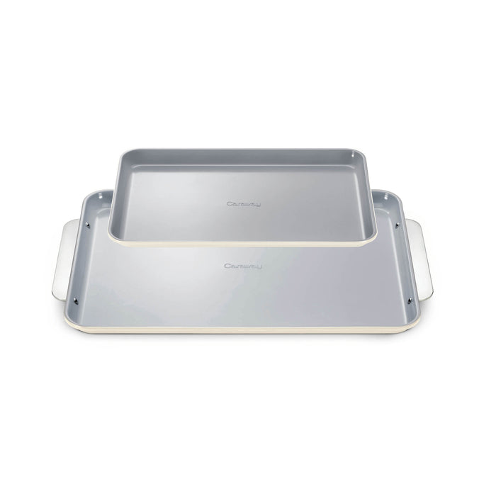 The Caraway Ceramic Baking Sheet Duo features two overlapping sheets with white edges and light gray, naturally non-stick surfaces, complete with extended side handles for easy grip. They boast a non-toxic design perfect for healthy baking and are set against a white background.