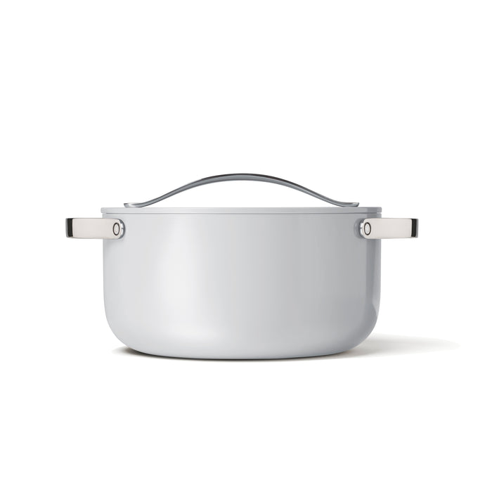 The Caraway Ceramic Dutch Oven, 6.5 qt, features a white ceramic coating with silver handles and lid. This non-toxic, naturally non-stick pot sits elegantly on a white surface against a plain background for effortless cooking.