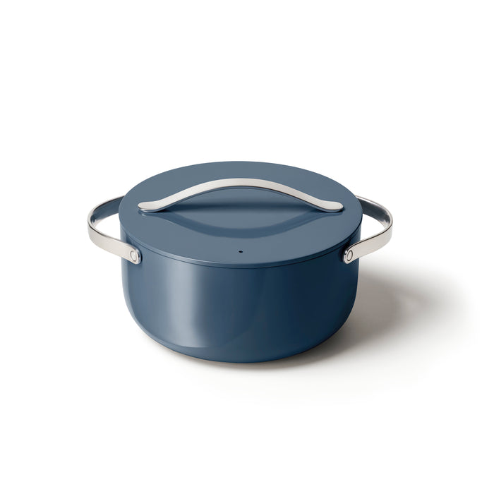 The Caraway Ceramic Dutch Oven, 6.5 qt, is a sleek blue pot with a smooth finish, metal handles, and a lid with a curved handle. Set against a white background, its design ensures its naturally non-stick and non-toxic for the perfect cooking experience.