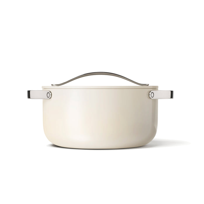 The Caraway Ceramic Dutch Oven, 6.5 qt, features a sleek white ceramic-coated design with a metal handle and matching side handles against a plain white background, providing non-toxic benefits in a minimalist style.