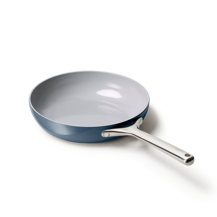 The Caraway Ceramic Fry Pan, 10.5, features a blue ceramic exterior and a shiny steel handle. Its naturally non-stick, non-toxic light gray ceramic-coated interior enhances its sleek design against a plain white background.