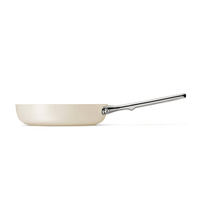 The Caraway Ceramic Fry Pan, 8, features a cream hue and a sleek stainless steel handle, positioned horizontally against a white background to highlight its minimalist and elegant design.