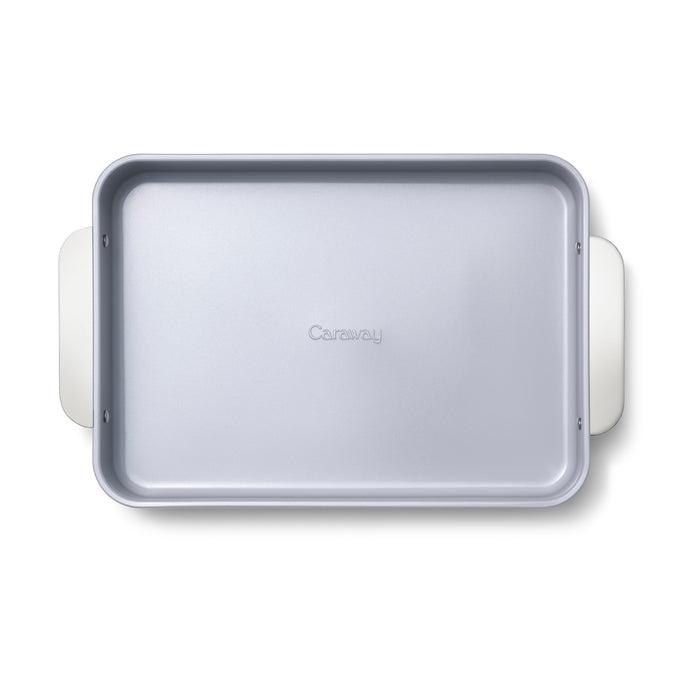 A top view of Caraways Ceramic Rectangle Baking Pan, light gray with rounded corners and wide white handles, features a non-toxic ceramic coating and the brand name embossed in the center. Ideal for healthy baking on a plain white background.
