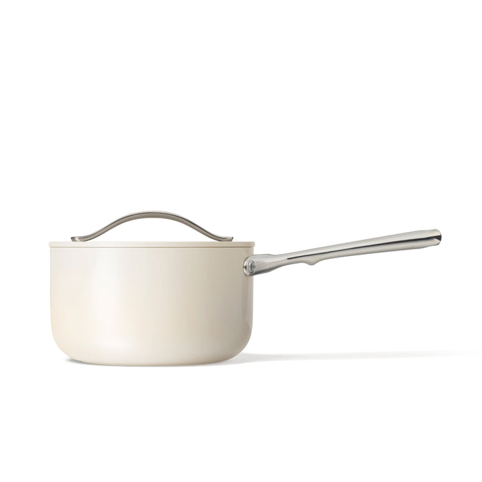 The Caraway 3 qt Ceramic Sauce Pan features a ceramic-coated, naturally non-stick interior with an elegant cream finish, a lid, and a long stainless steel handle. Its sleek modern design is highlighted against a plain white background.