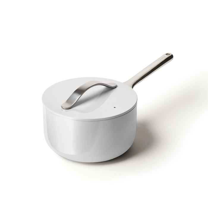 The Caraway Ceramic Sauce Pan, 3 qt, is displayed on a plain white background. This stylish white pan features a long stainless steel handle and a matching lid with a curved handle, embodying a modern and minimalistic design while prioritizing non-toxic materials.