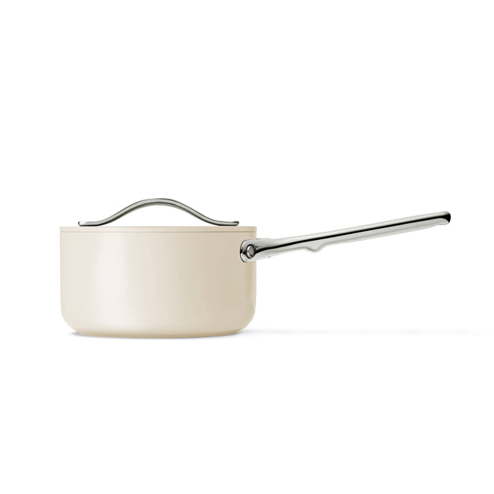 Displayed against a plain white background, the Caraway Ceramic Sauce Pan with Lid (1.75 qt) features a cream color, long silver handle, and matching lid. Its sleek design and non-stick surface make it ideal for modern, healthy cooking.