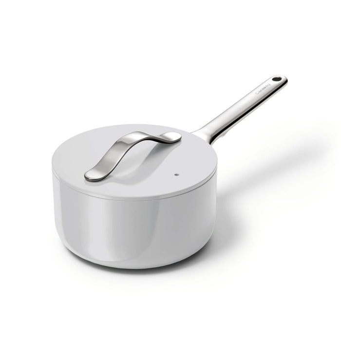 The Caraway Ceramic Sauce Pan with Lid, 1.75 qt, in sleek white, has a smooth metal handle and non-toxic coating, set against a plain backdrop.