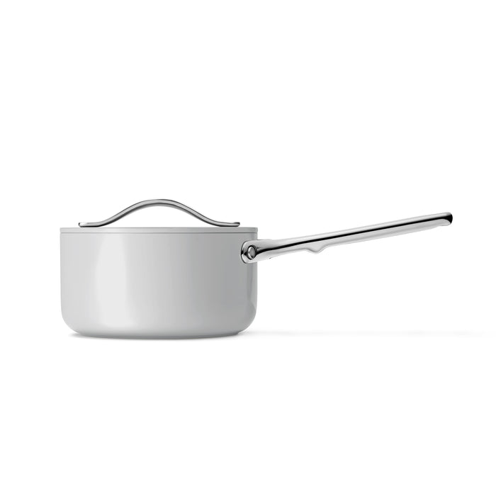 The Caraway Ceramic Sauce Pan with Lid, 1.75 qt, is a sleek white saucepan featuring a non-toxic coating and shiny stainless steel handle. Its smooth surface ensures healthy cooking and includes a matching lid, all set against a plain white background.