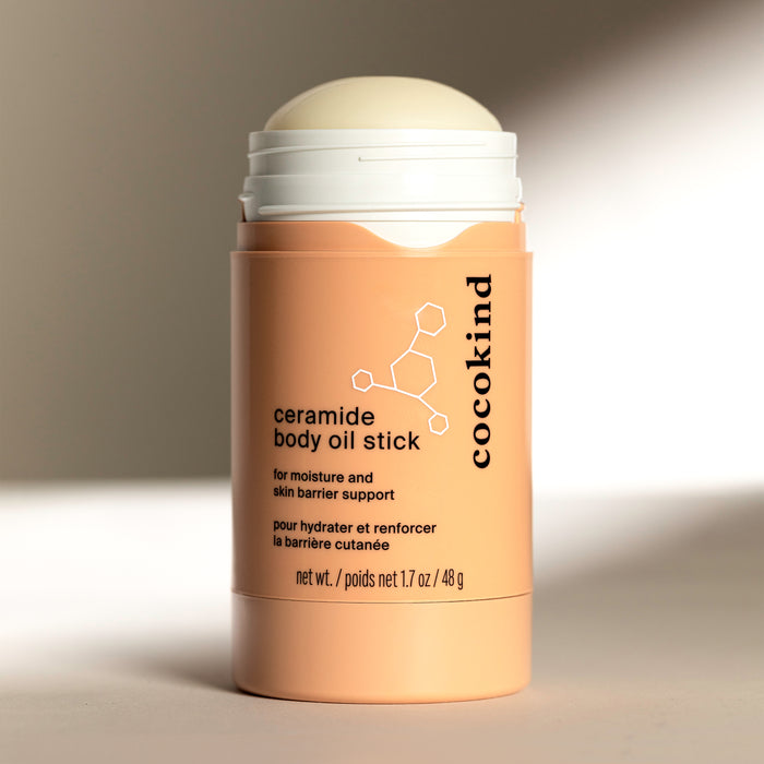 Cocokinds peach-colored Ceramide Body Oil Stick showcases a rounded product in an open container. The fragrance-free formula is highlighted for its moisturizing and skin barrier support benefits.