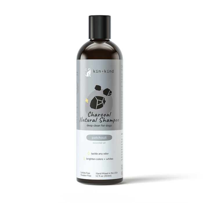 A bottle of kin+kind Charcoal Deep Clean Natural Shampoo for dogs features a grey label highlighting patchouli oils benefits, such as odor control and color brightening. The sleek design includes a black cap, providing gentle care with activated charcoal.