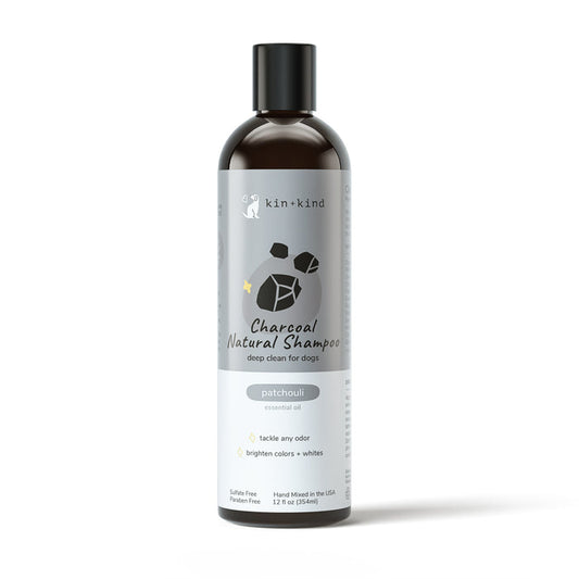 A bottle of kin+kind Charcoal Deep Clean Natural Shampoo for dogs features a grey label highlighting patchouli oils benefits, such as odor control and color brightening. The sleek design includes a black cap, providing gentle care with activated charcoal.