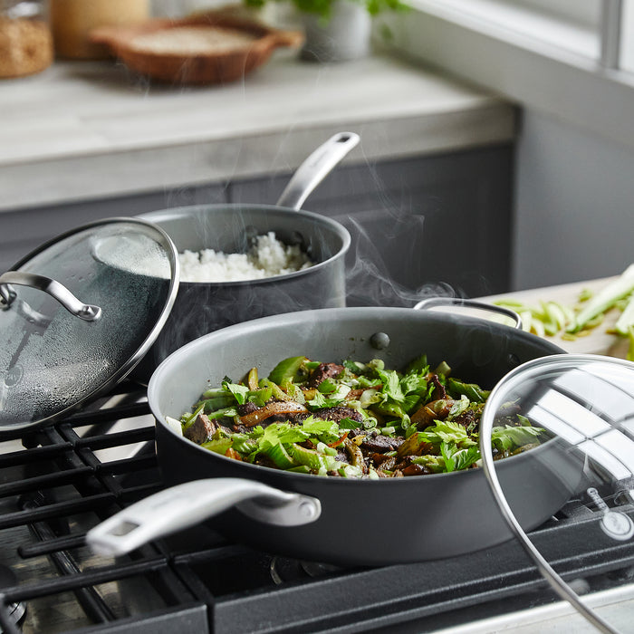 In a sunlit kitchen, two pots from GreenPans Chatham Ceramic, Non-Stick Cookware Set sit atop the stove—one brimming with steaming rice, the other with vibrant vegetables and herbs—ensuring healthy cooking without harmful chemicals.