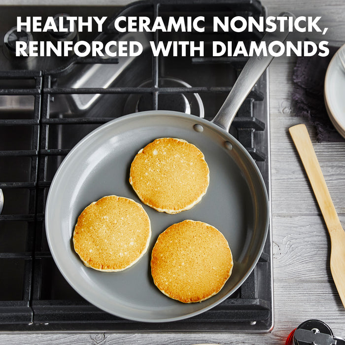A GreenPan Chatham 12" ceramic nonstick frypan with three golden pancakes sits on a gas stove. Text reads: Healthy ceramic nonstick, diamond-reinforced. A spatula and plate rest nearby on the wood countertop. PFAS free for safer cooking.