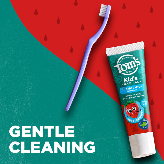 Purple toothbrush and tube of Tom's fluoride-free kid's toothpaste with a strawberry design on the packaging, placed on a red and green split background. The words "Gentle Cleaning" are written in white text.