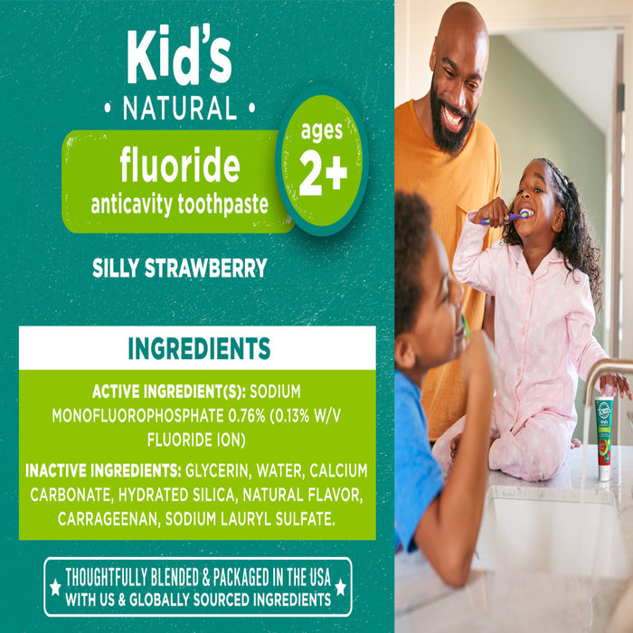 A smiling man helps a child brush their teeth with kid's natural fluoride toothpaste, suitable for ages 2 and up. The toothpaste has a silly strawberry flavor. The image highlights active ingredients and mentions it is made in the USA.