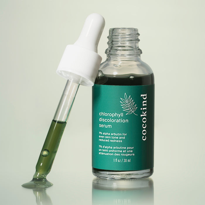 A clear glass bottle filled with green liquid, labeled Chlorophyll Discoloration Serum by Cocokind, stands upright. A dropper sits beside it. The label emphasizes improving skin tone and reducing redness, making it ideal for fading spots in your skincare routine.